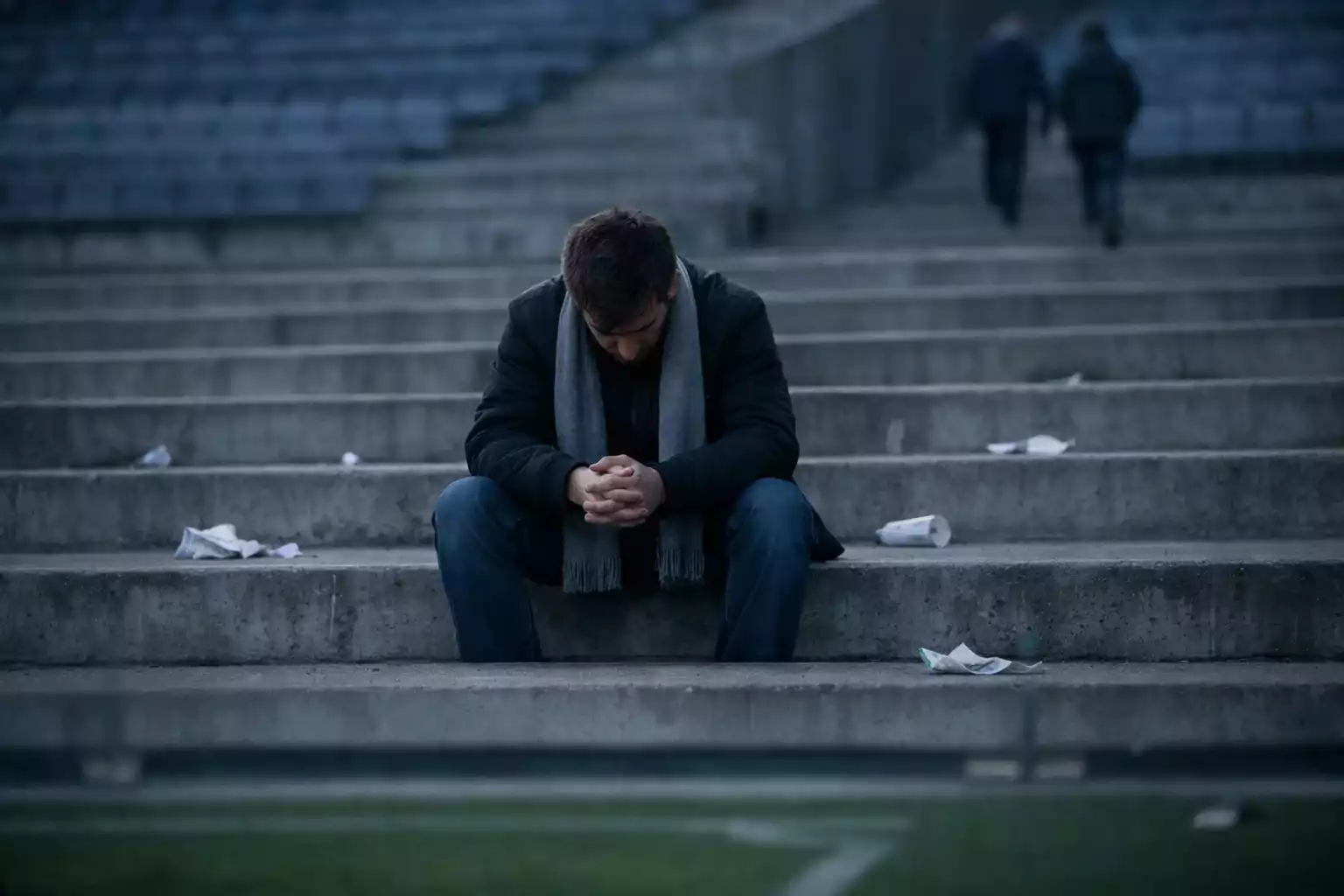 Tifoso di calcio deluso seduto sulle gradinate vuote di uno stadio a fine partita